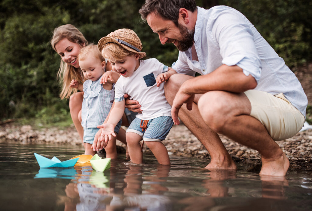 Familie am Fluss mit Papierschiffen schwimmen. Mhr mit der Familie zu unternehmen ist für viele ein guter Vorsatz.