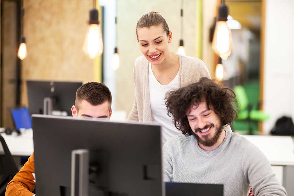 Frau macht einem Arbeitskollegen vor seinem Computerbildschirm ein Kompliment zu seiner Arbeit.