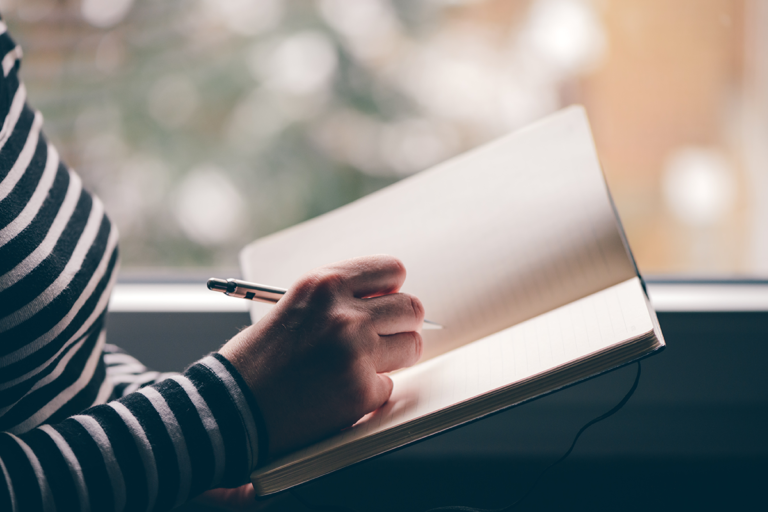 Frau hält ein offenes Buch mit leeren Seiten in der Hand, um ihre guten Vorsätze zu notieren.